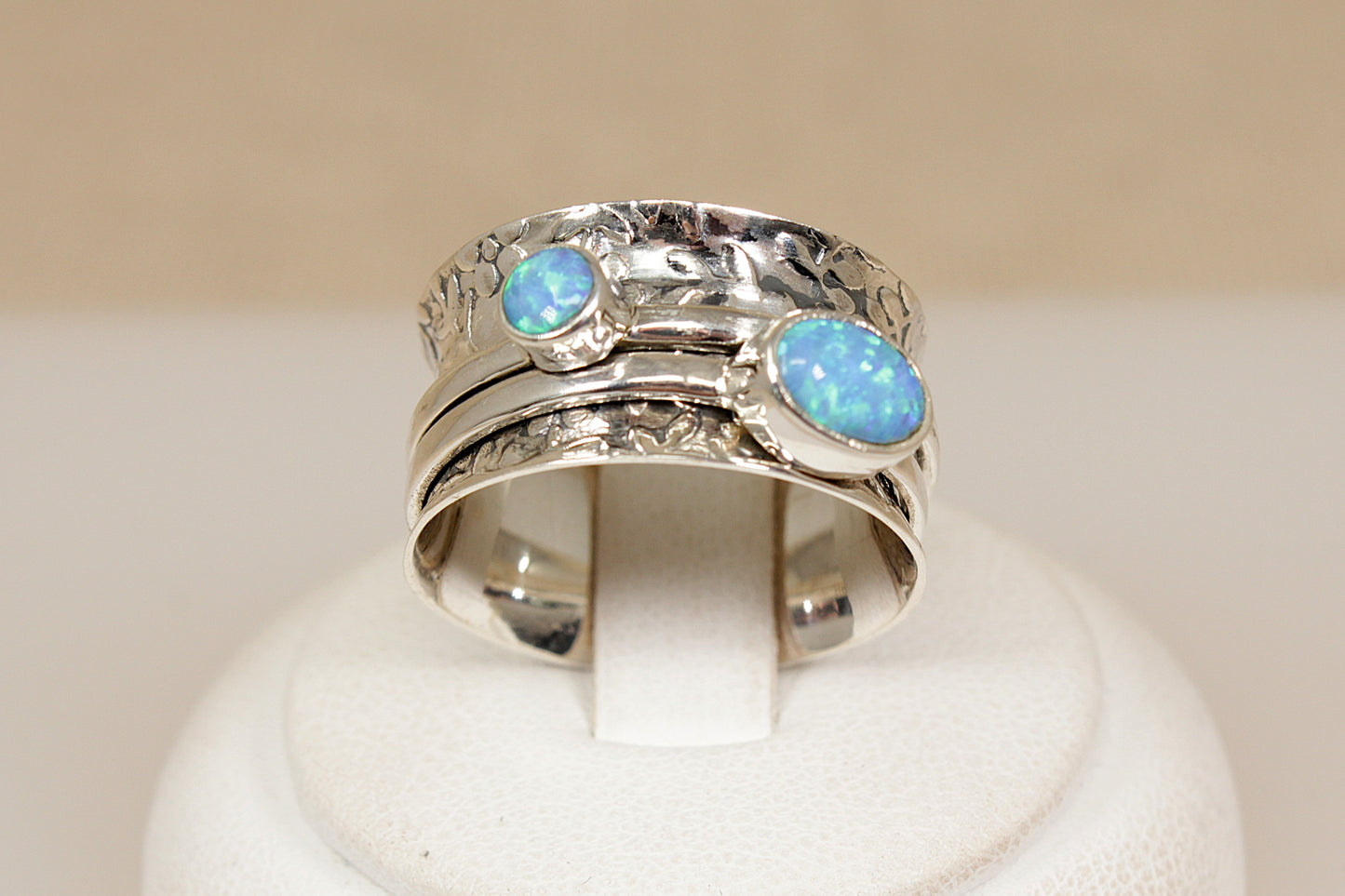 Silver ring with opal stones on a white stand against a beige background
