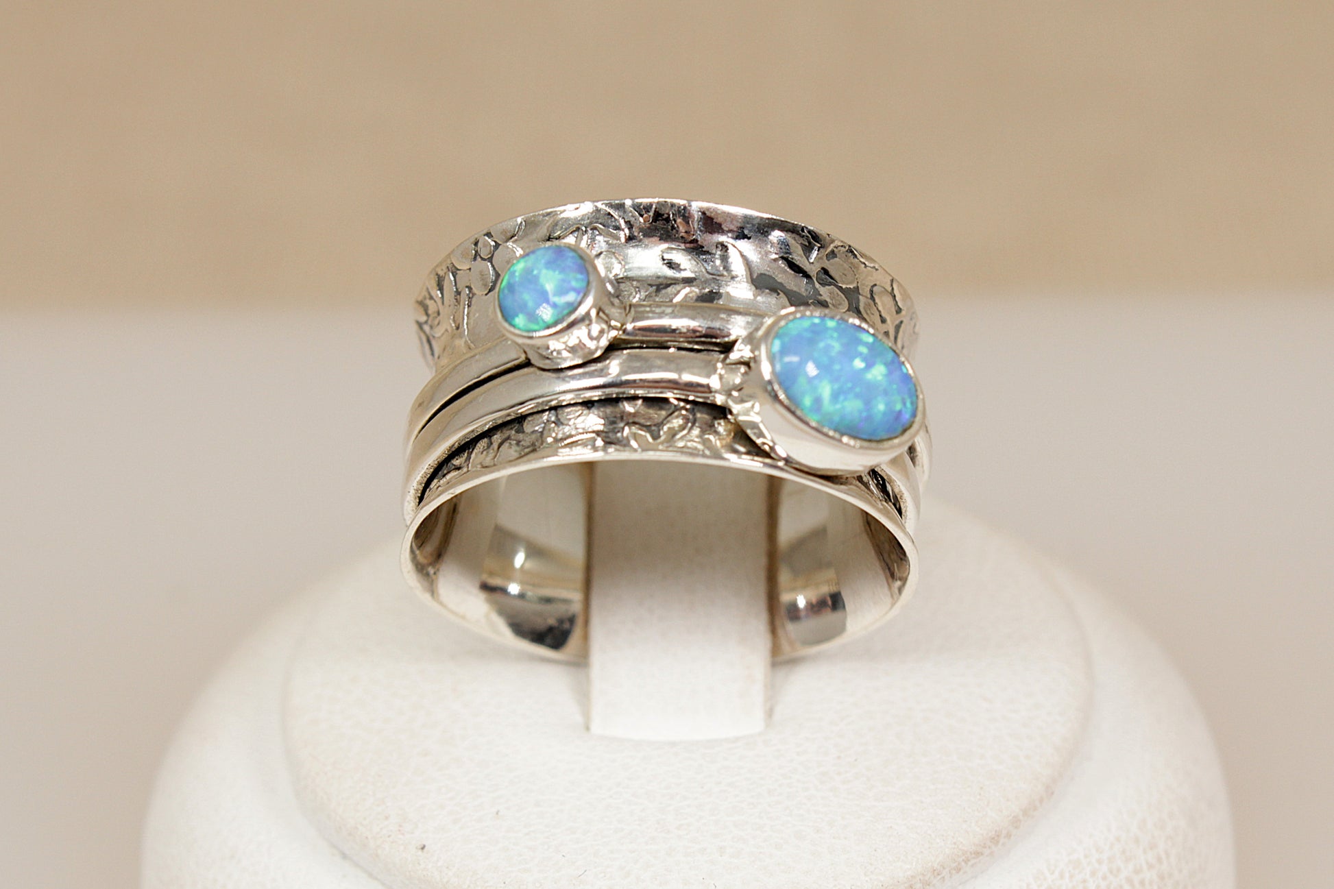 Silver ring with opal stones on a white stand against a beige background