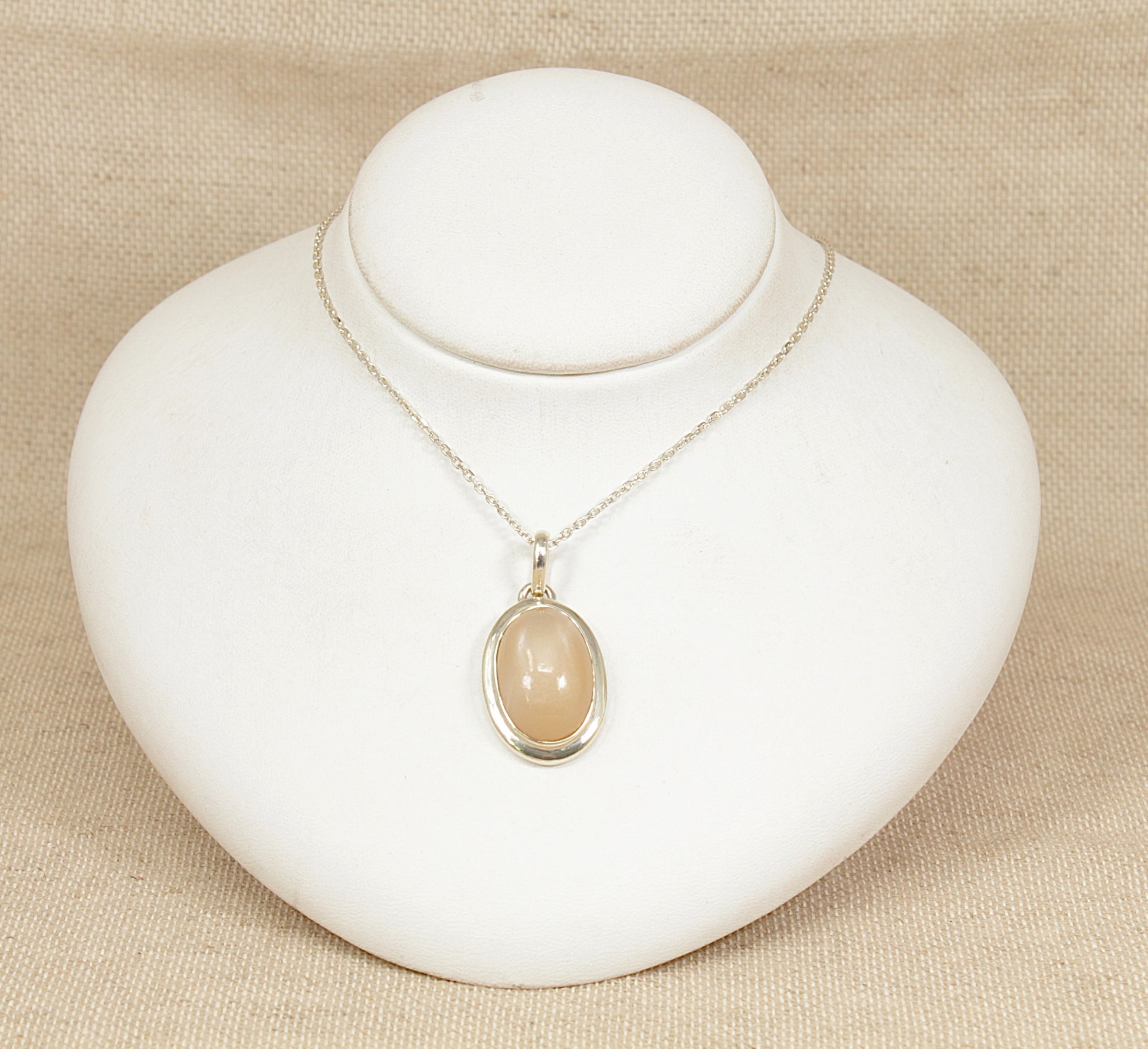Necklace with a peach moonstone  pendant on a white stand against a beige background
