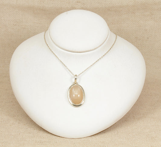 Necklace with a peach moonstone  pendant on a white stand against a beige background