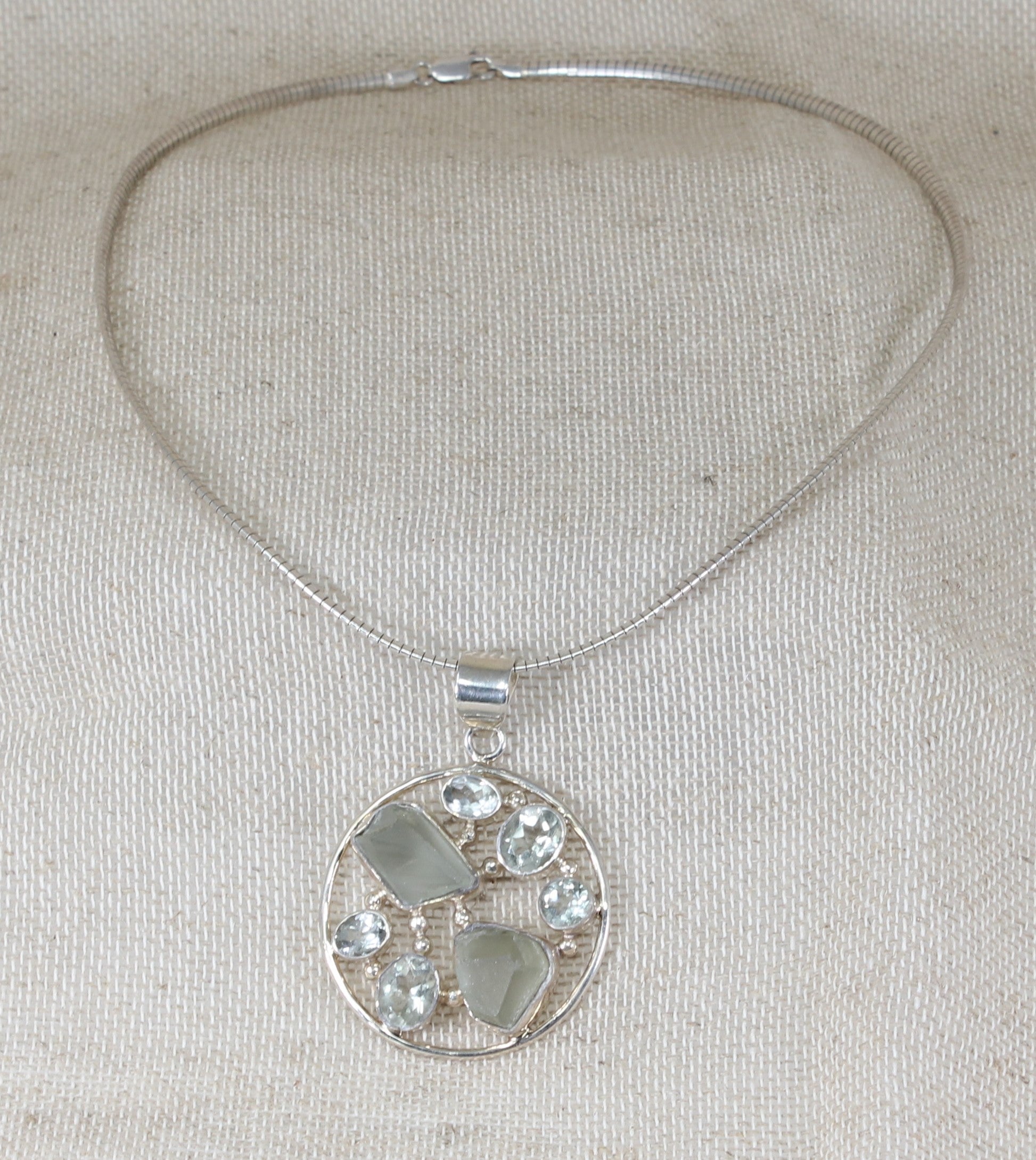 This gorgeous Silver collarette has a large round handcrafted pendant inset with faceted and raw Quartz gemstones in an asymmetric design. Made in Italy, this statement pendant sits on a snake chain collarette. Pendant size: 42mm round.