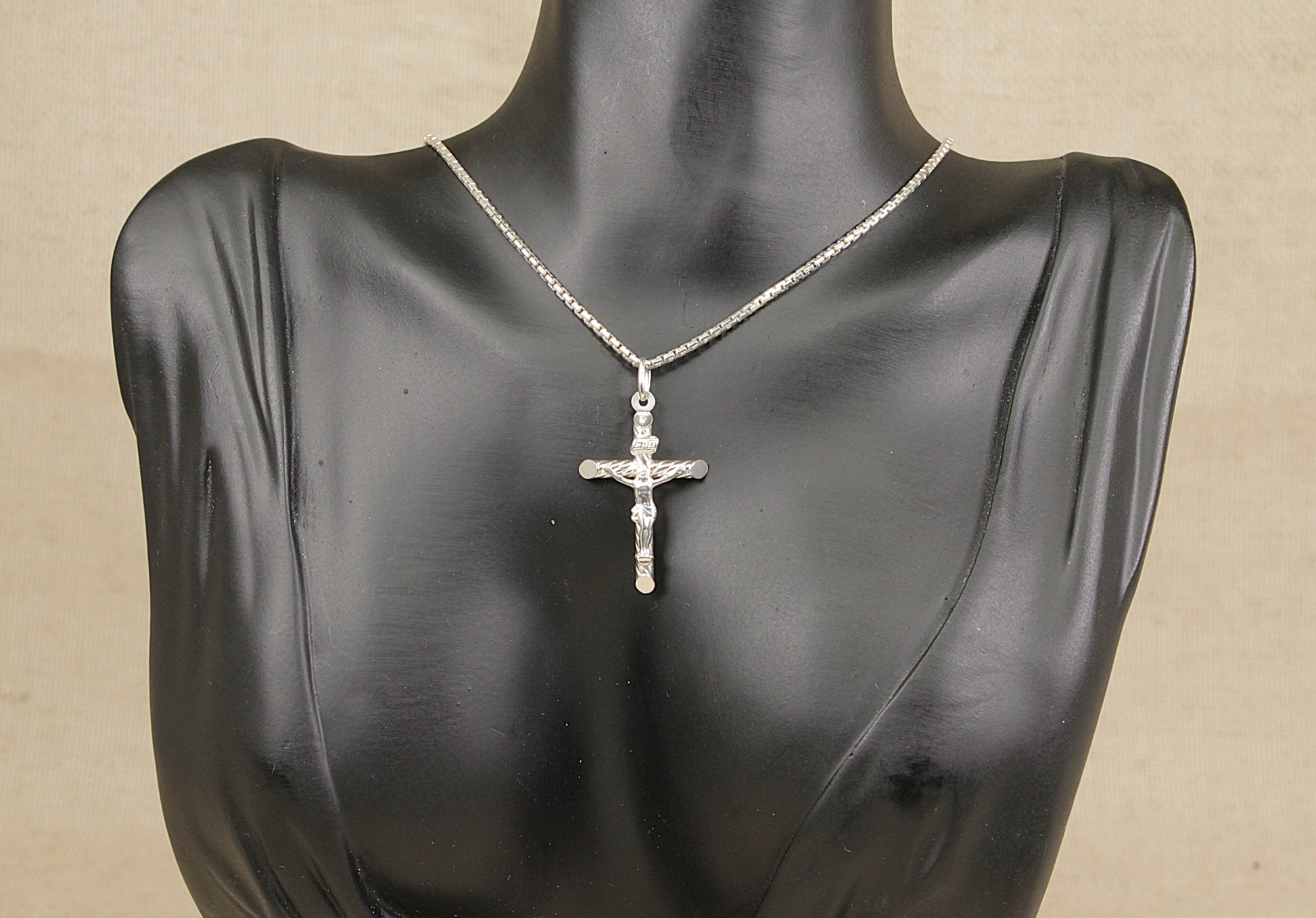 A sterling silver cross pendant necklace displayed on a mannequin bust.