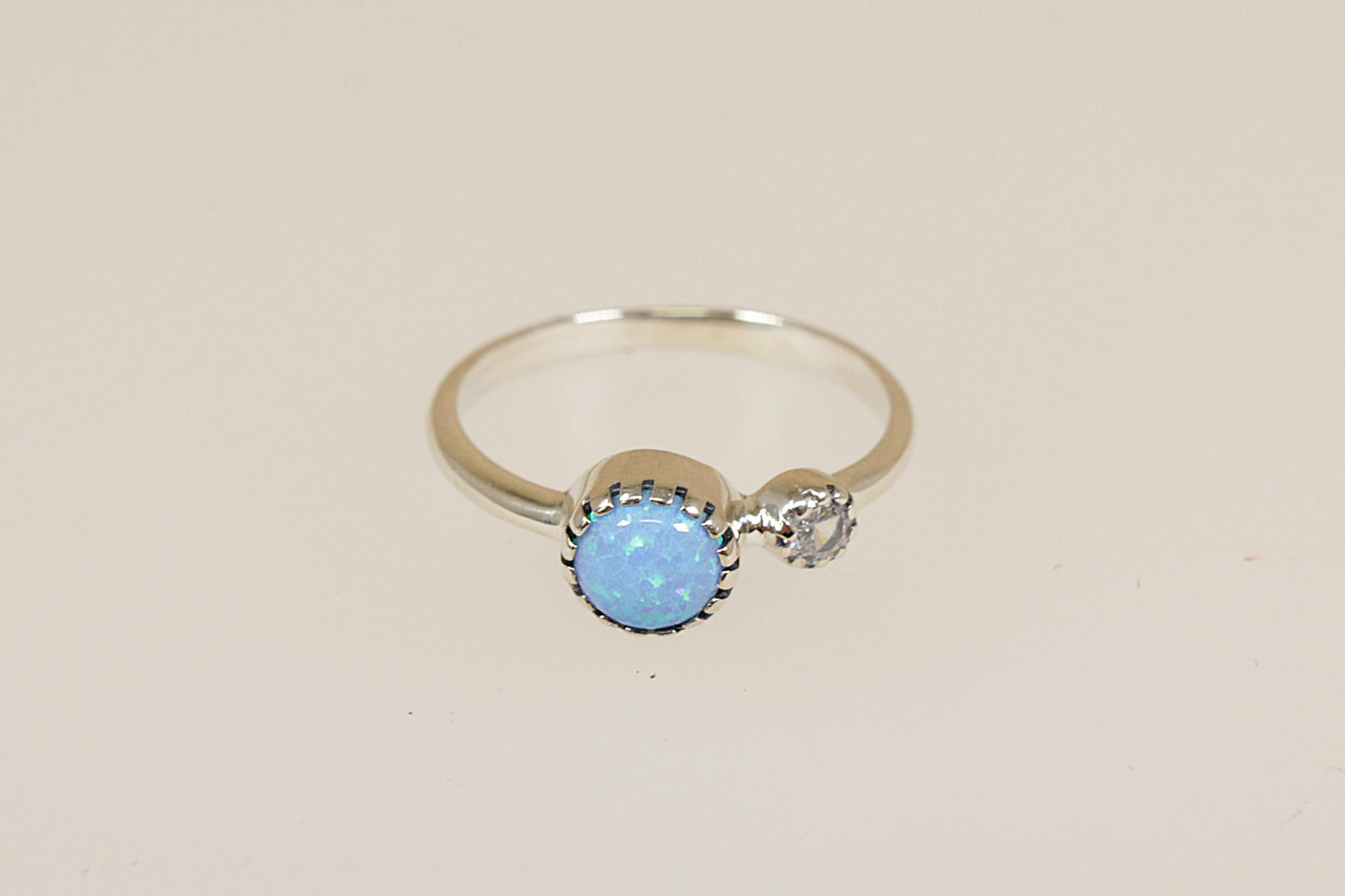 Silver ring with a blue opal and crystal gemstones on a beige background 