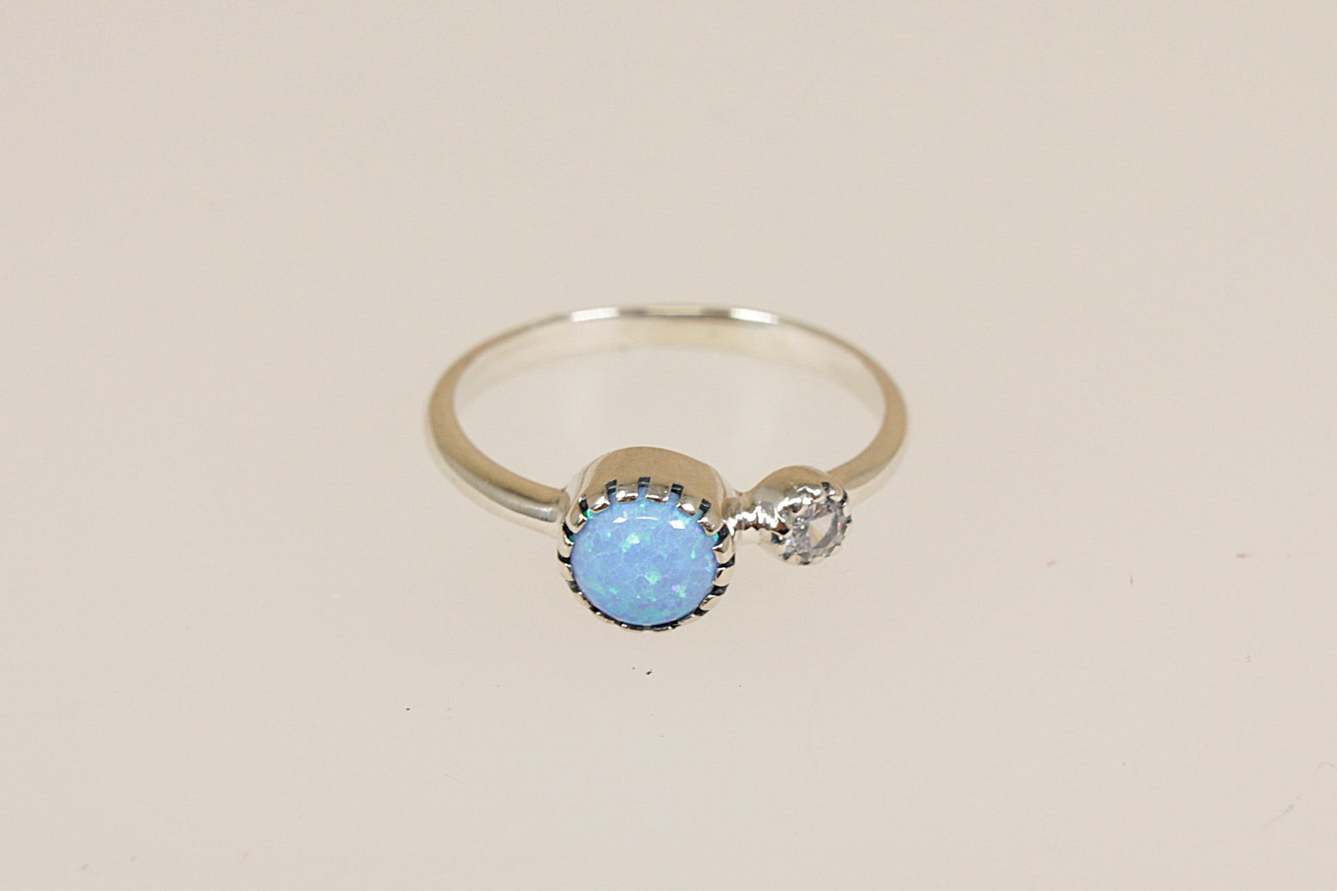 Silver ring with a blue opal and crystal gemstones on a beige background 