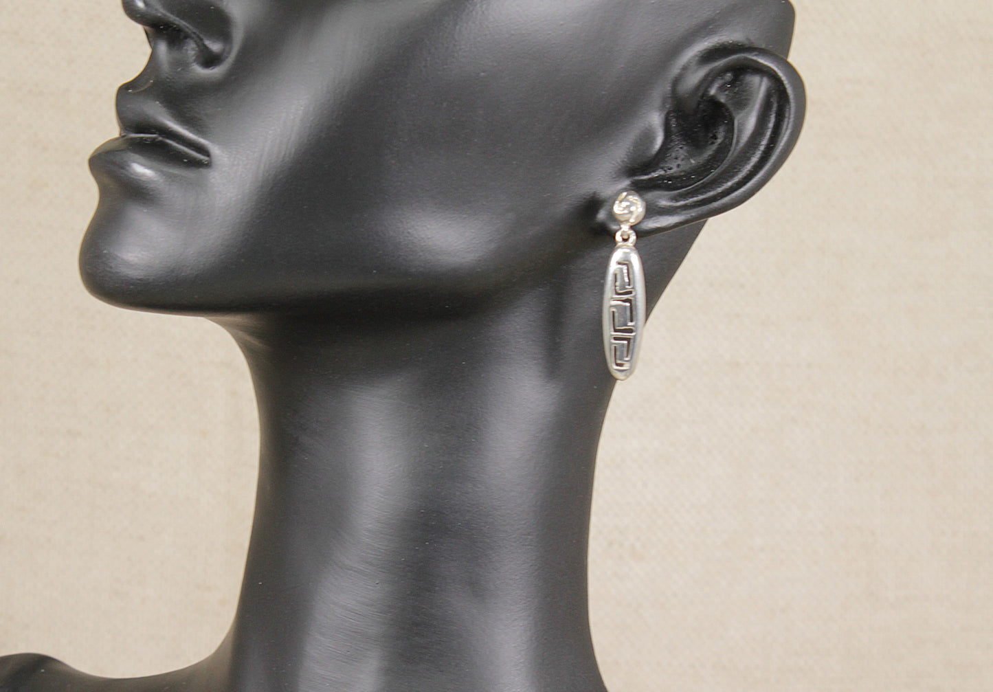 Mannequin head wearing a silver earring on a beige background