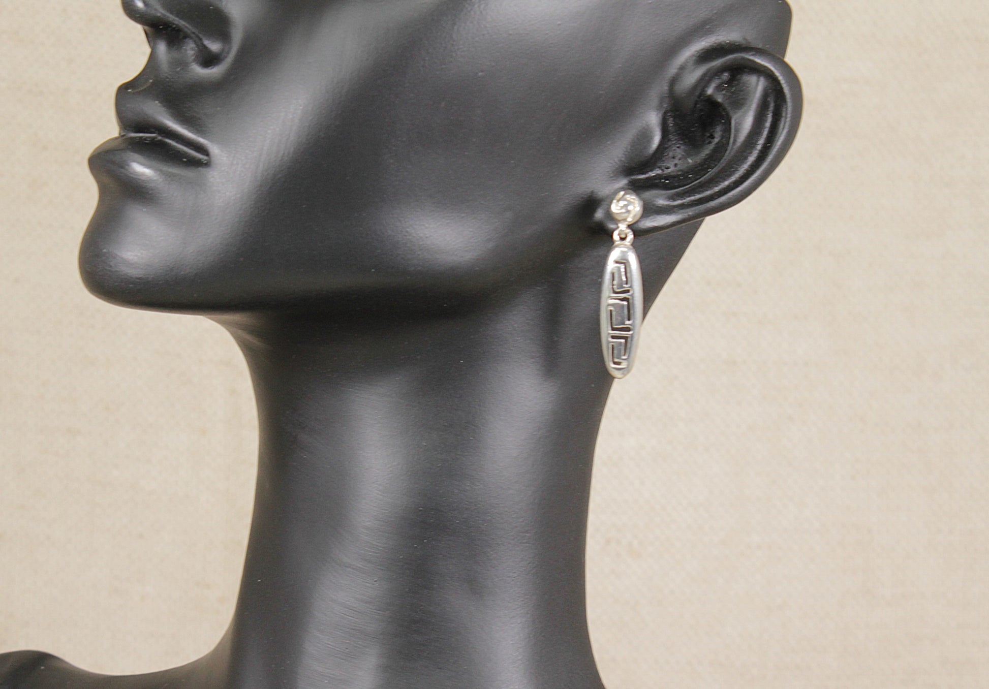 Mannequin head wearing a silver earring on a beige background