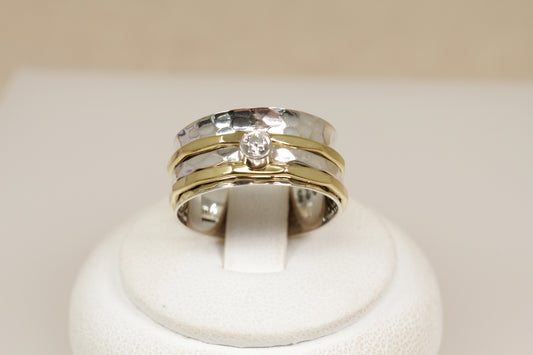A stylish new Silver spinner ring, two gold colour bands and one silver with white gemstone on a white stand with a beige background. 