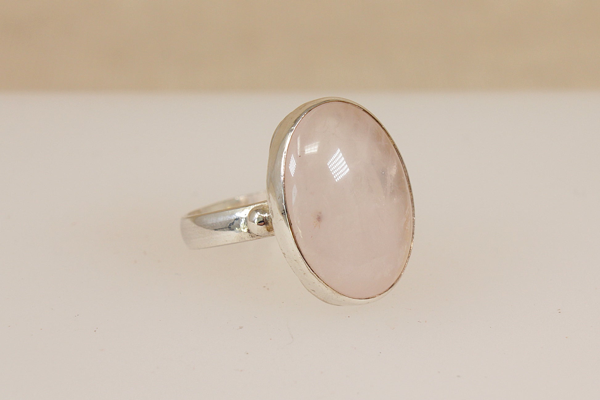 Silver ring with a pink rainbow moonstone gemstone on a beige background