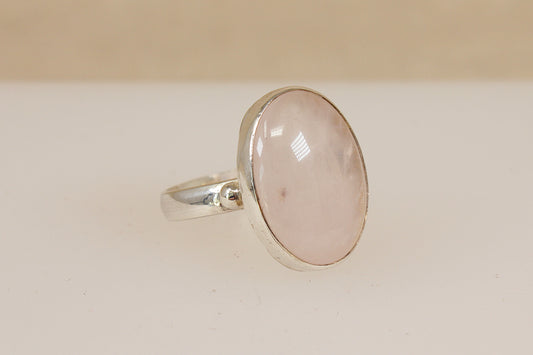 Silver ring with a pink rainbow moonstone gemstone on a beige background