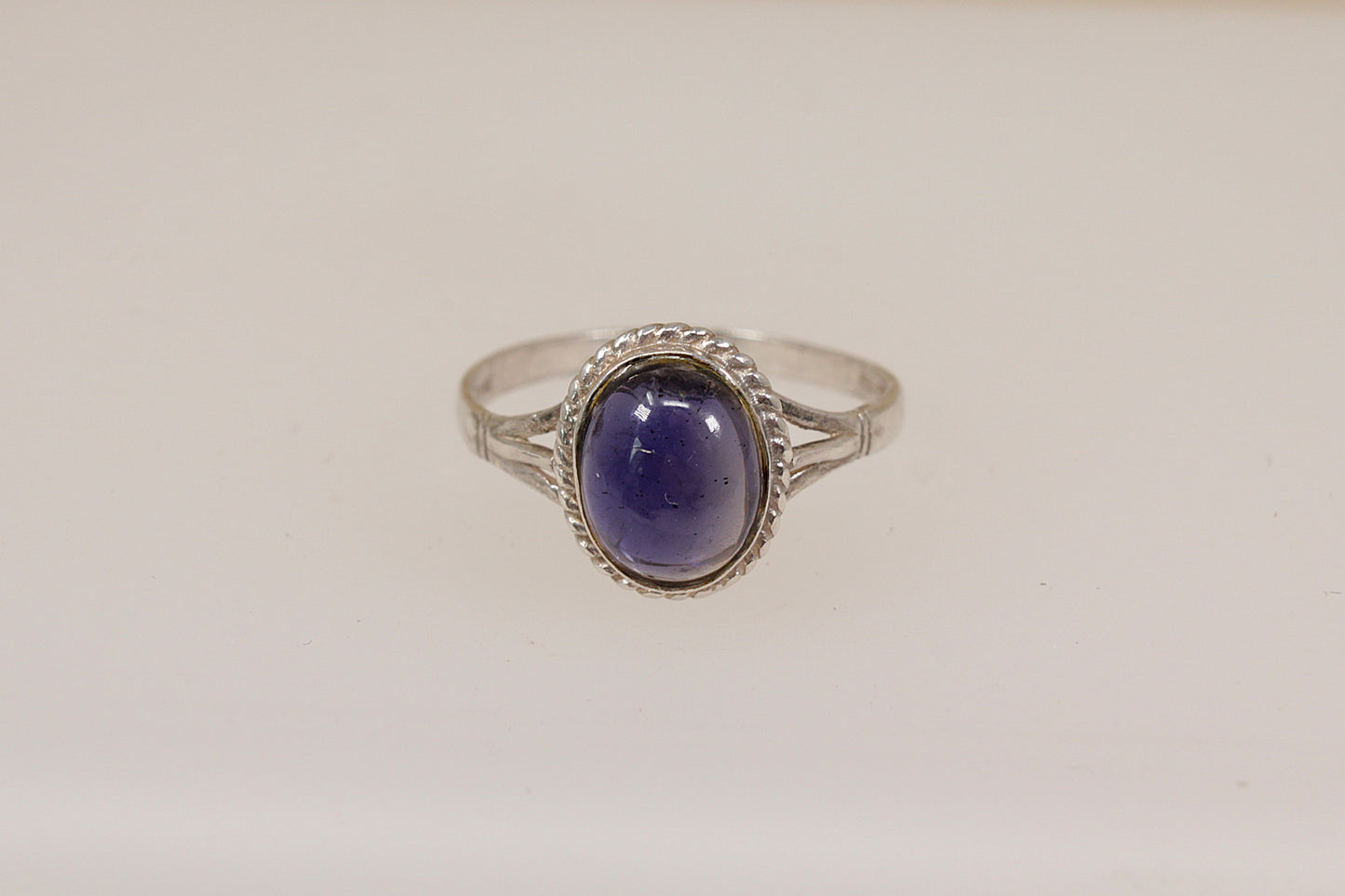 Silver ring with a purple iolite gemstone on a light beige background