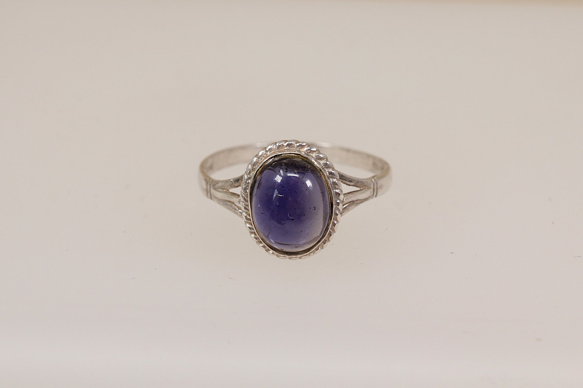 Silver ring with a purple iolite gemstone on a light beige background