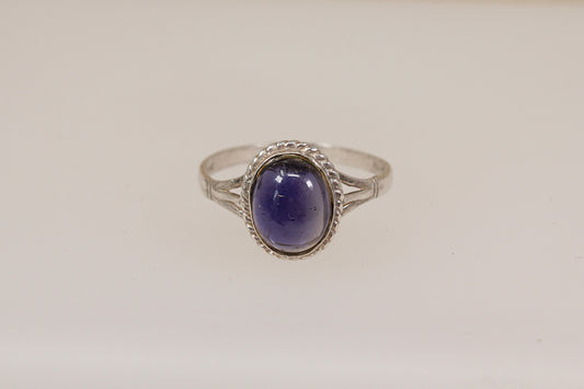 Silver ring with a purple iolite gemstone on a light beige background
