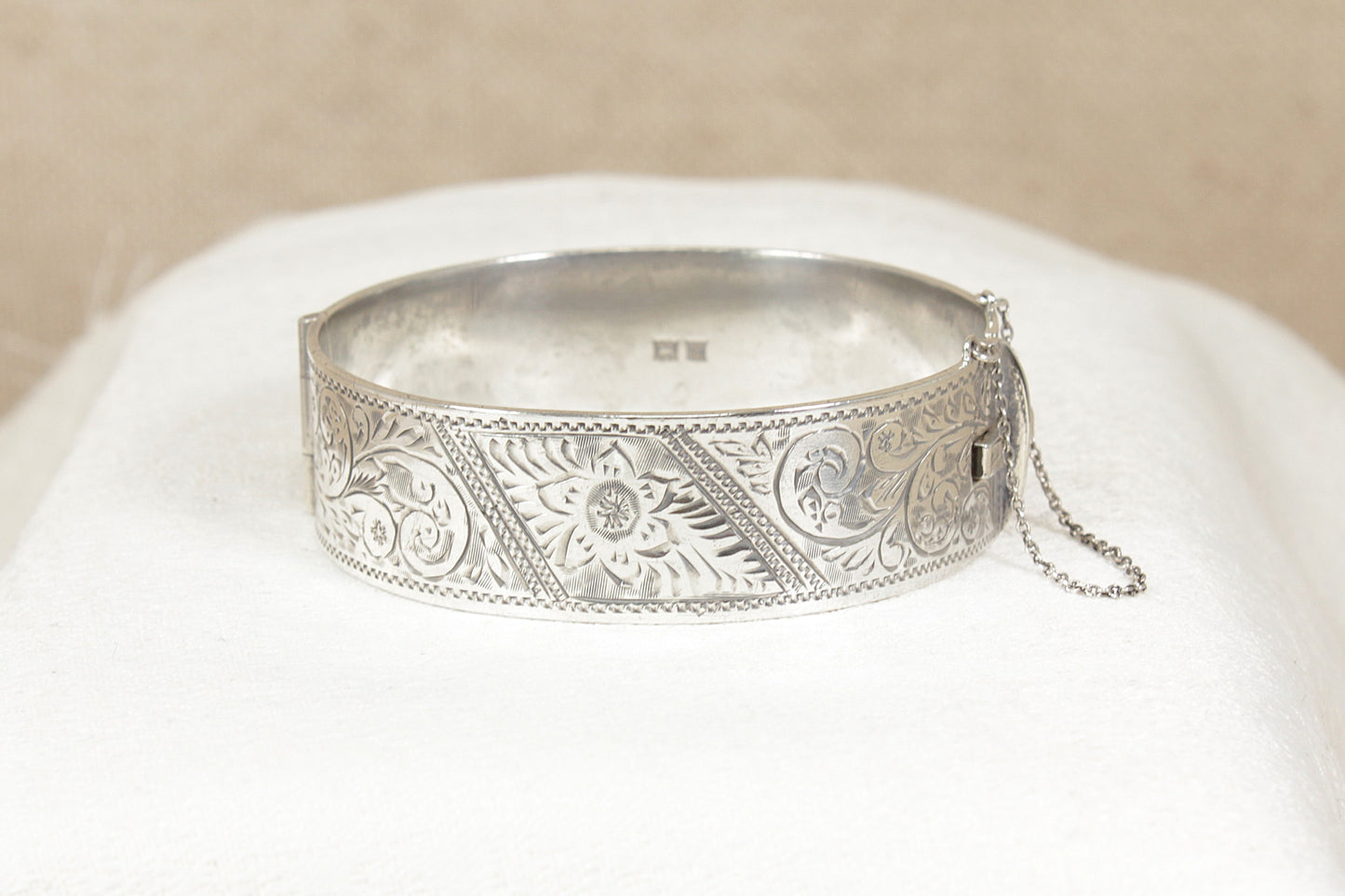 Vintage 1960's Silver bracelet bangle with intricate designs on a white cushion against a beige background