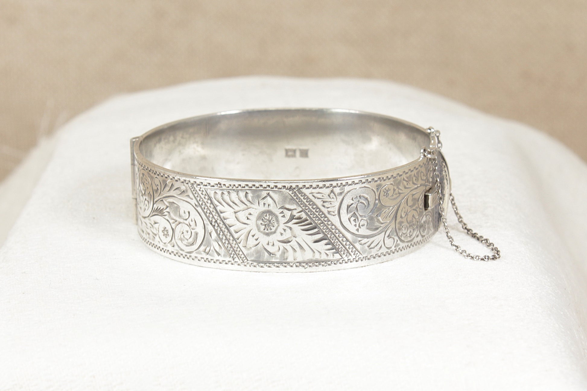 Vintage 1960's Silver bracelet bangle with intricate designs on a white cushion against a beige background
