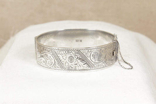 Vintage 1960's Silver bracelet bangle with intricate designs on a white cushion against a beige background