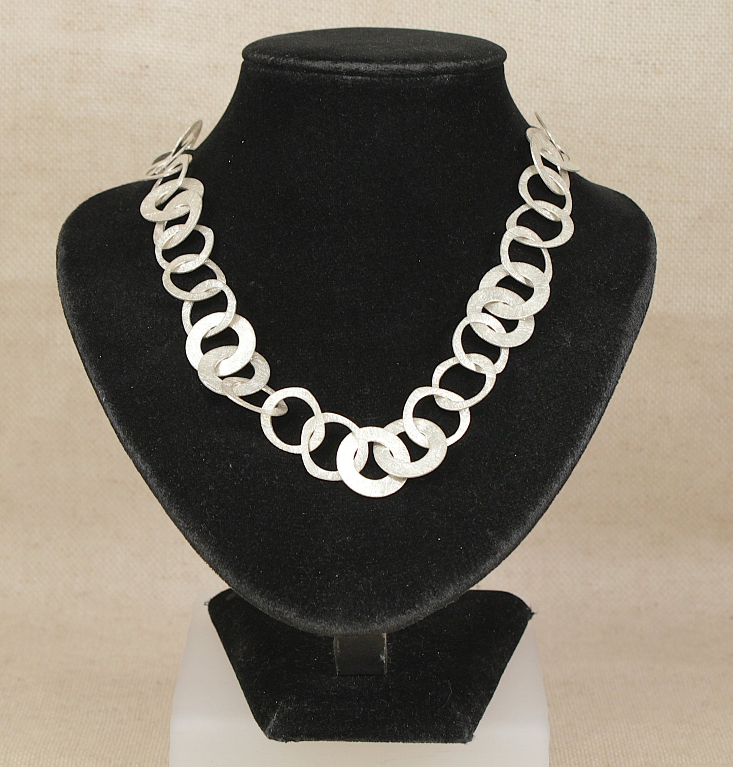 Silver chain designer necklace on a black velvet stand against a beige background