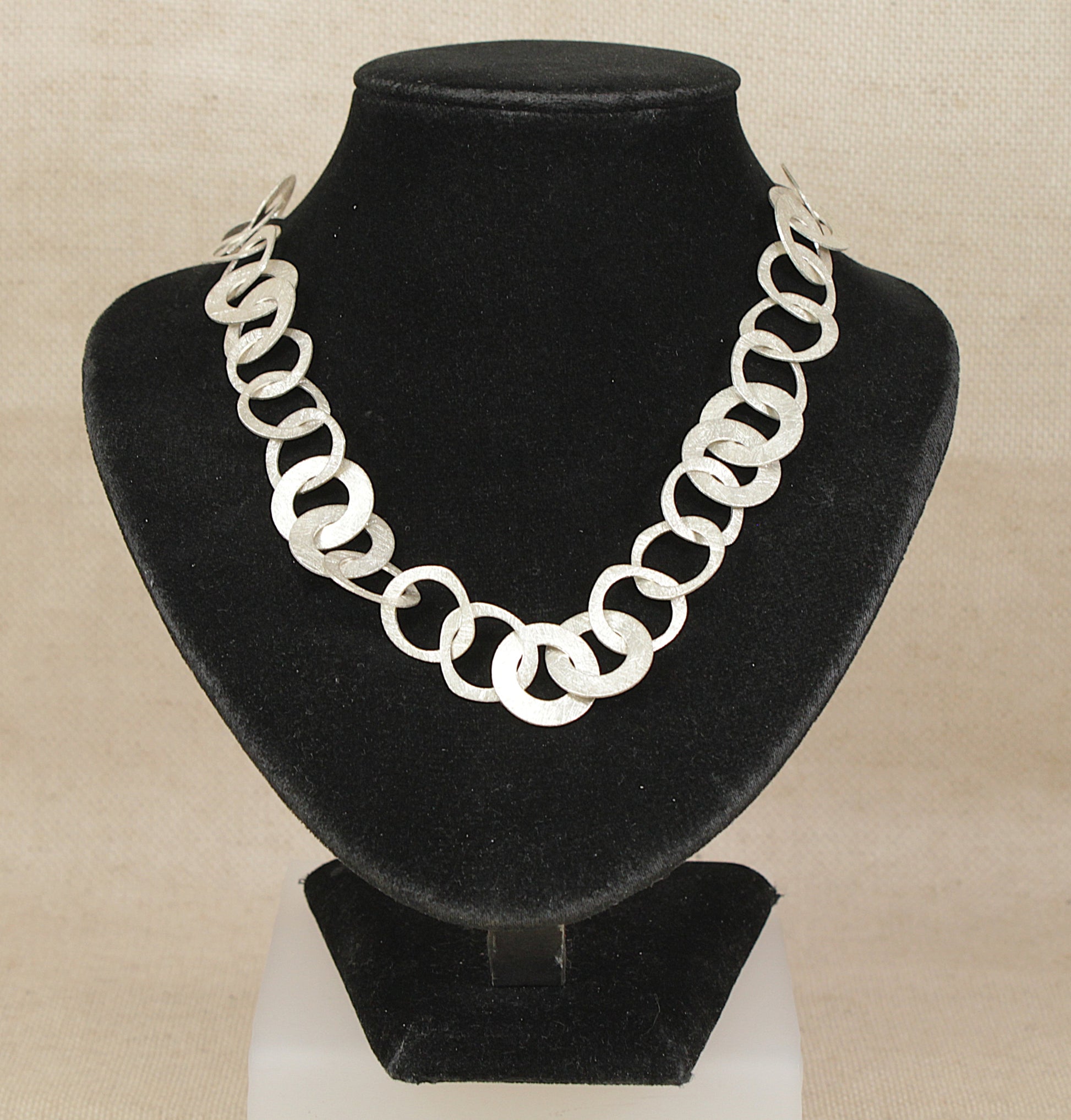 Silver chain designer necklace on a black velvet stand against a beige background