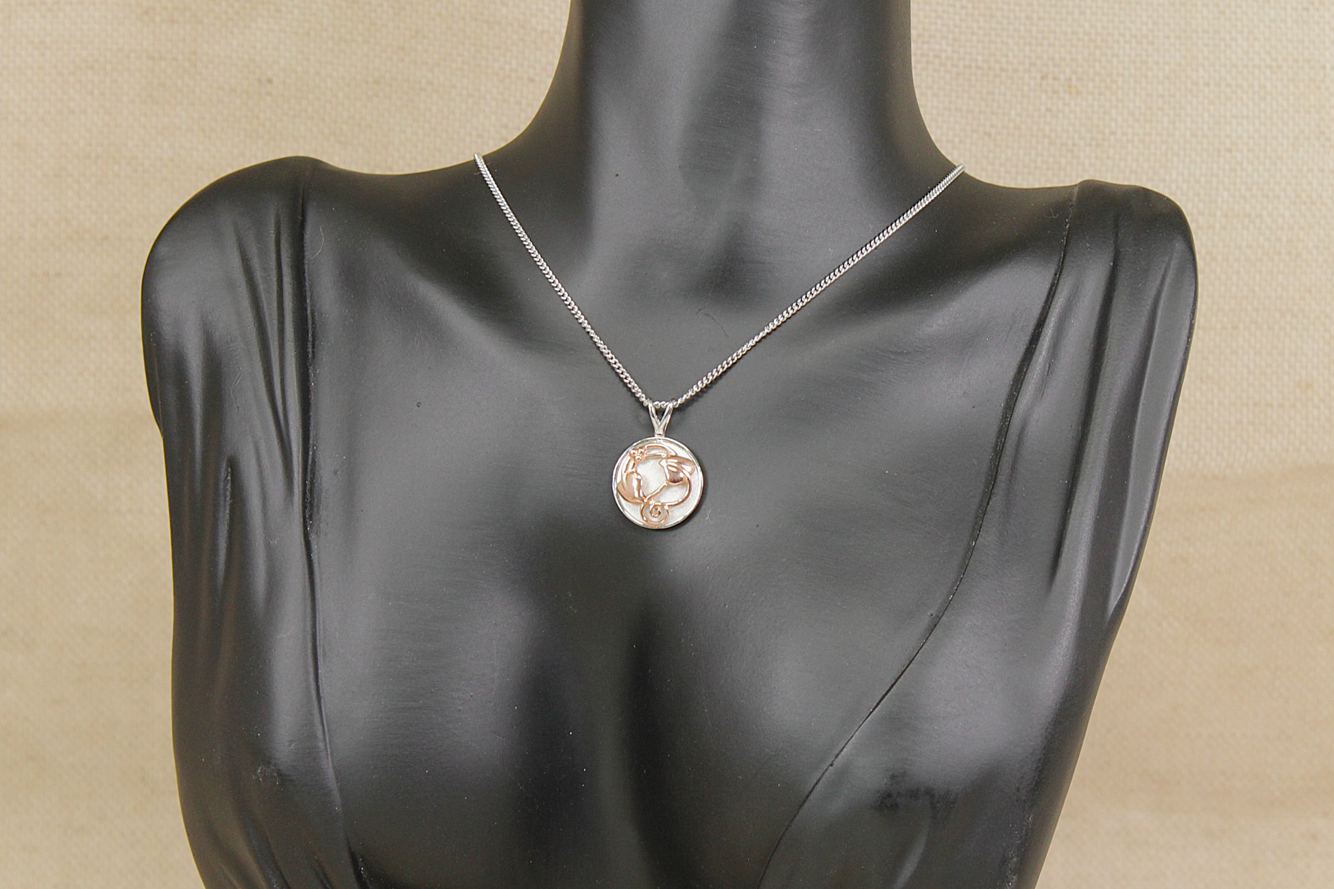 Necklace with a clogau silver and welsh gold pendant on a black mannequin bust against a beige background