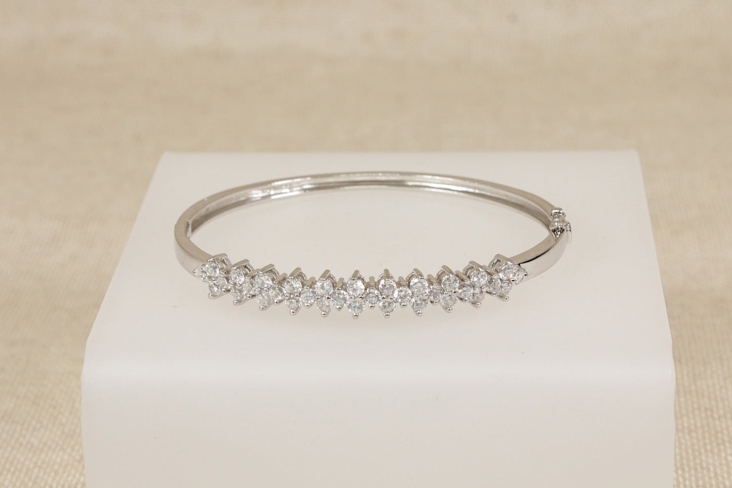 Silver bracelet with cubic zirconia  (diamond simulant) gemstones on a white cube against a beige background 
