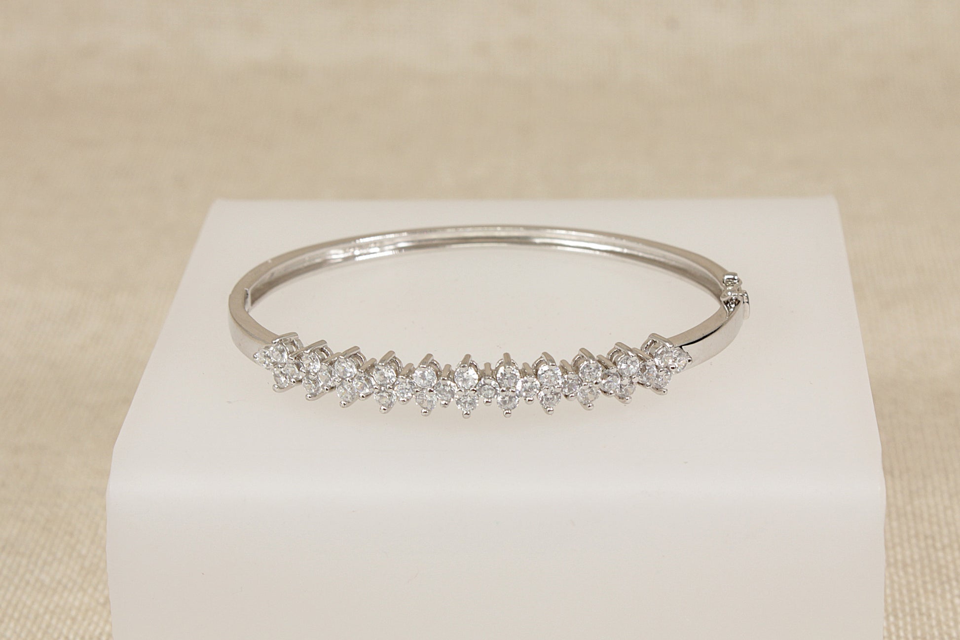 Silver bracelet with cubic zirconia  (diamond simulant) gemstones on a white cube against a beige background 