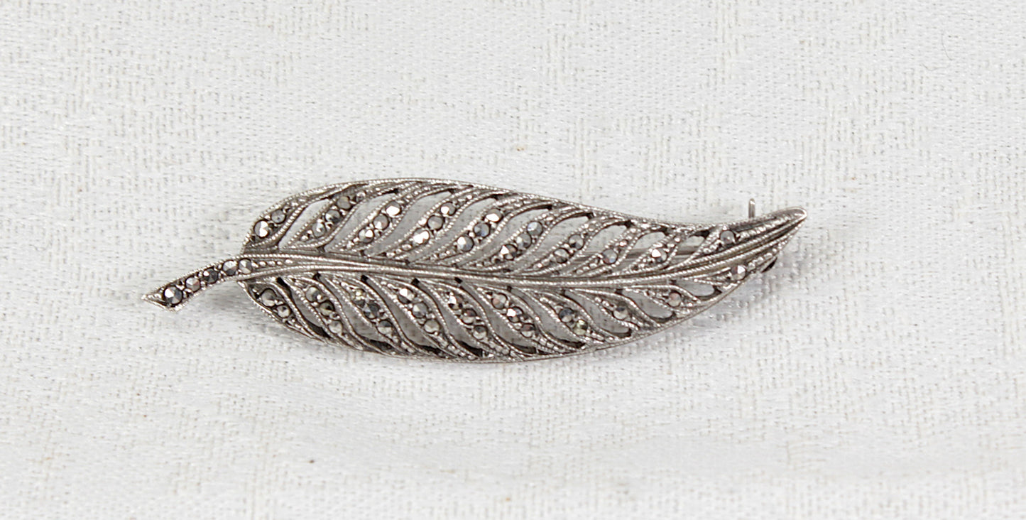 Silver feather-shaped vintage antique marcasite  brooch on a white fabric background