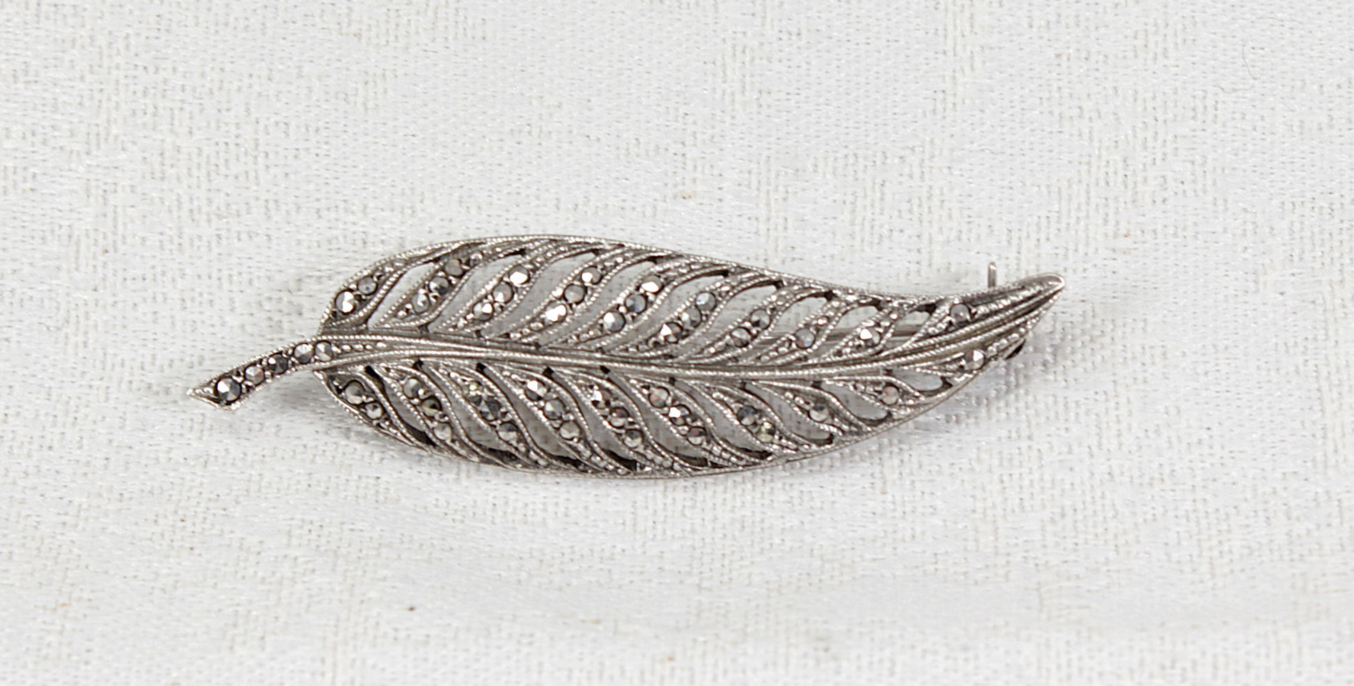 Silver feather-shaped vintage antique marcasite  brooch on a white fabric background