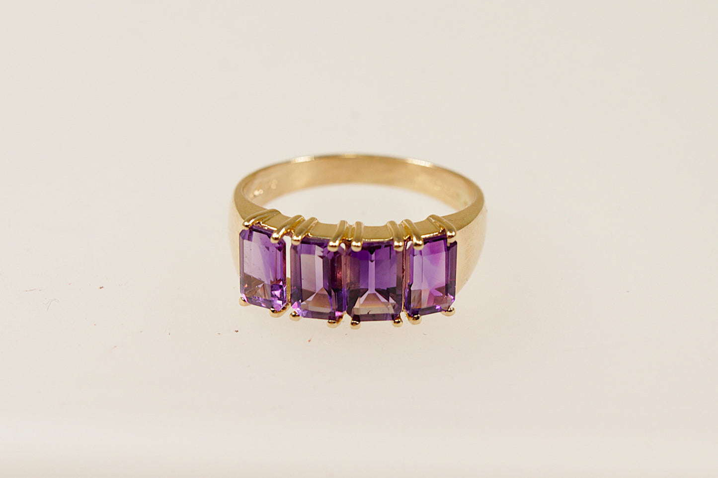 A vintage 14ct gold ring with four emerald cut Amethysts, featuring a yellow metal band and a 4 claw crown setting.