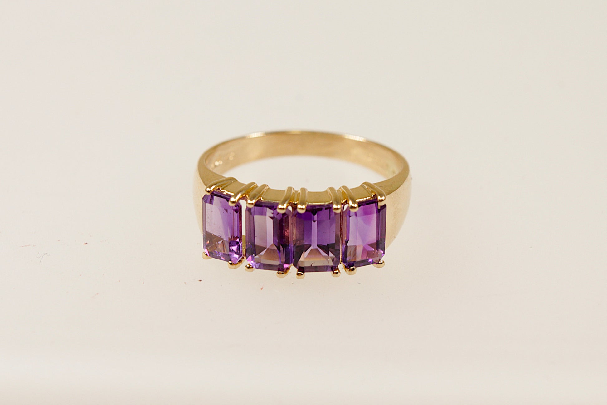 A vintage 14ct gold ring with four emerald cut Amethysts, featuring a yellow metal band and a 4 claw crown setting.