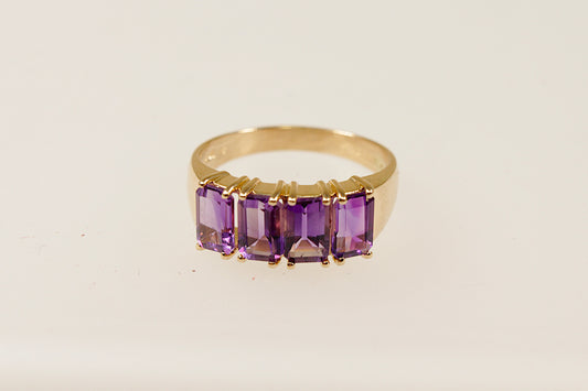 A vintage 14ct gold ring with four emerald cut Amethysts, featuring a yellow metal band and a 4 claw crown setting.