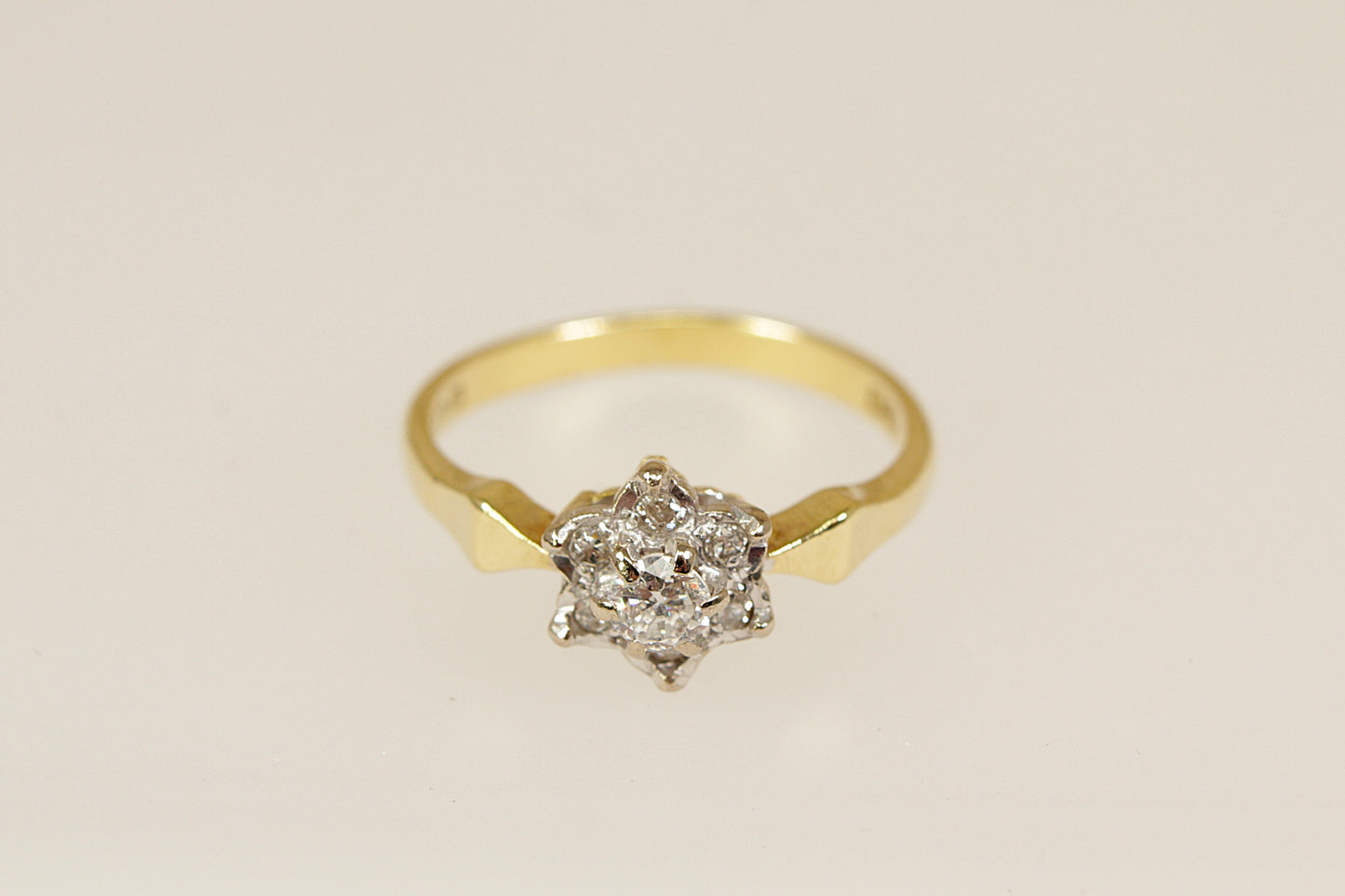 Gold ring with a diamond cluster on a beige background