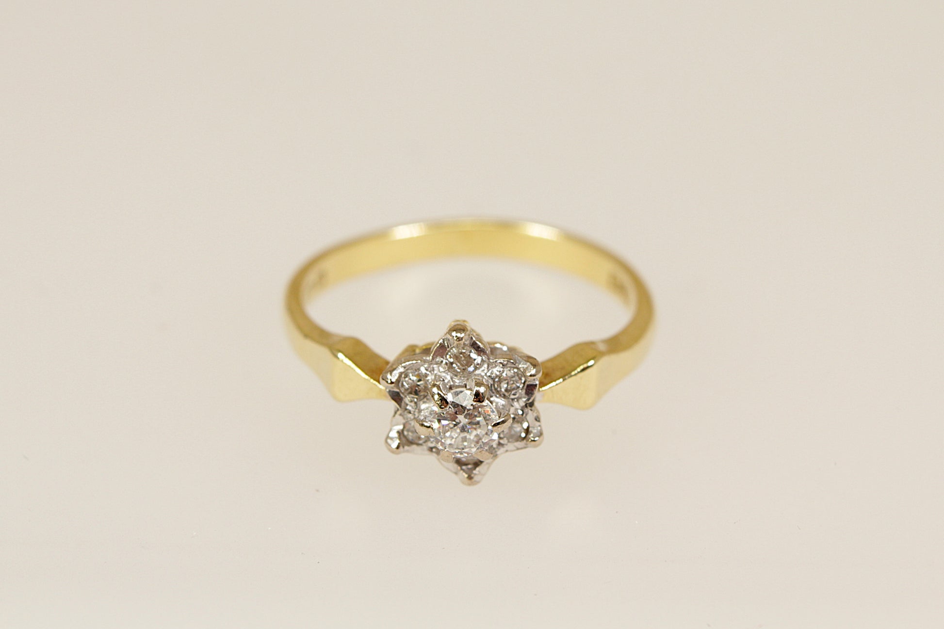 Gold ring with a diamond cluster on a beige background