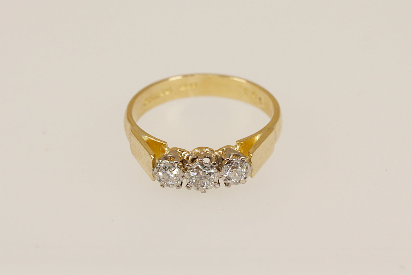Gold ring with three diamonds on a beige background