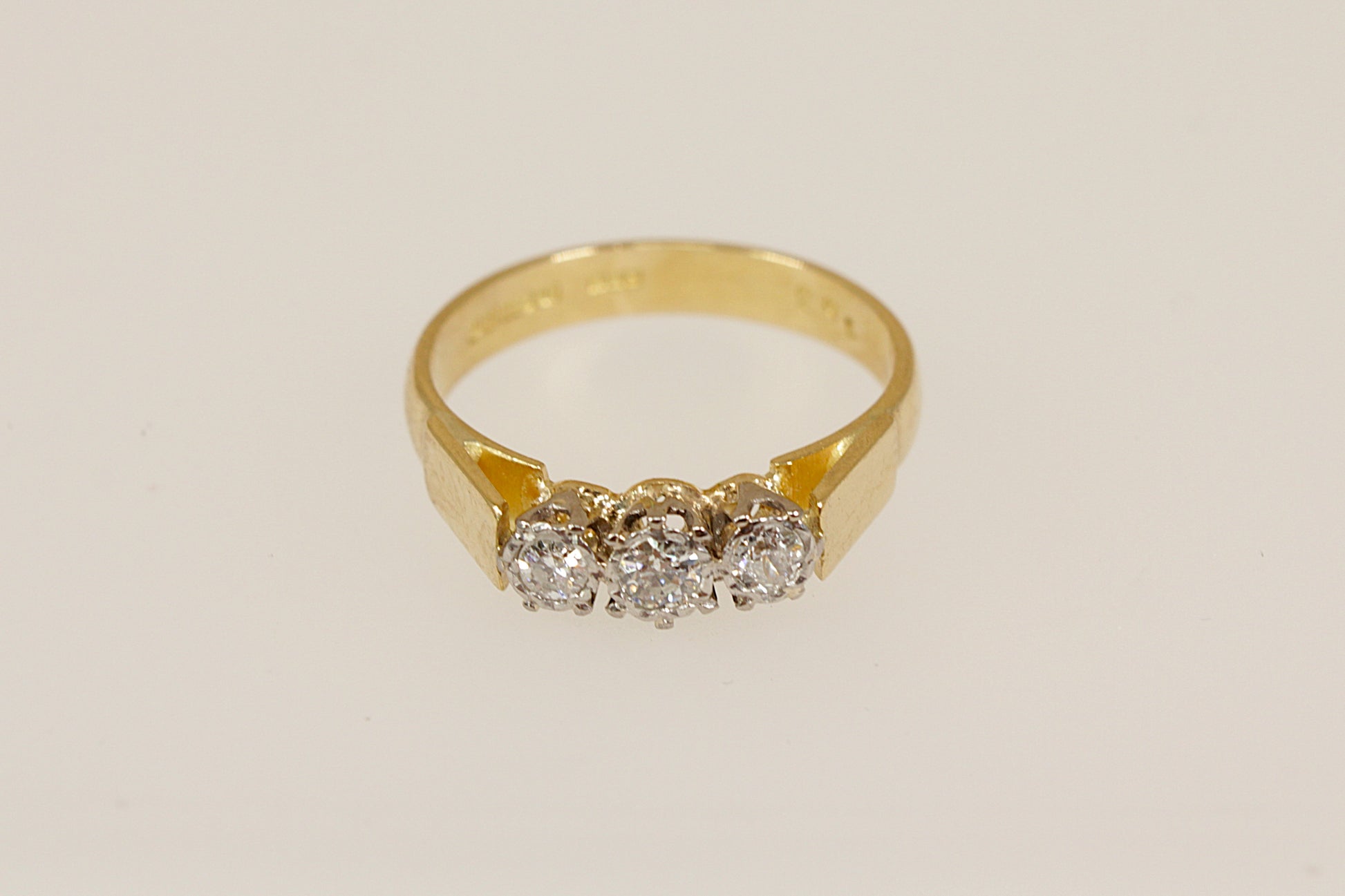 Gold ring with three diamonds on a beige background