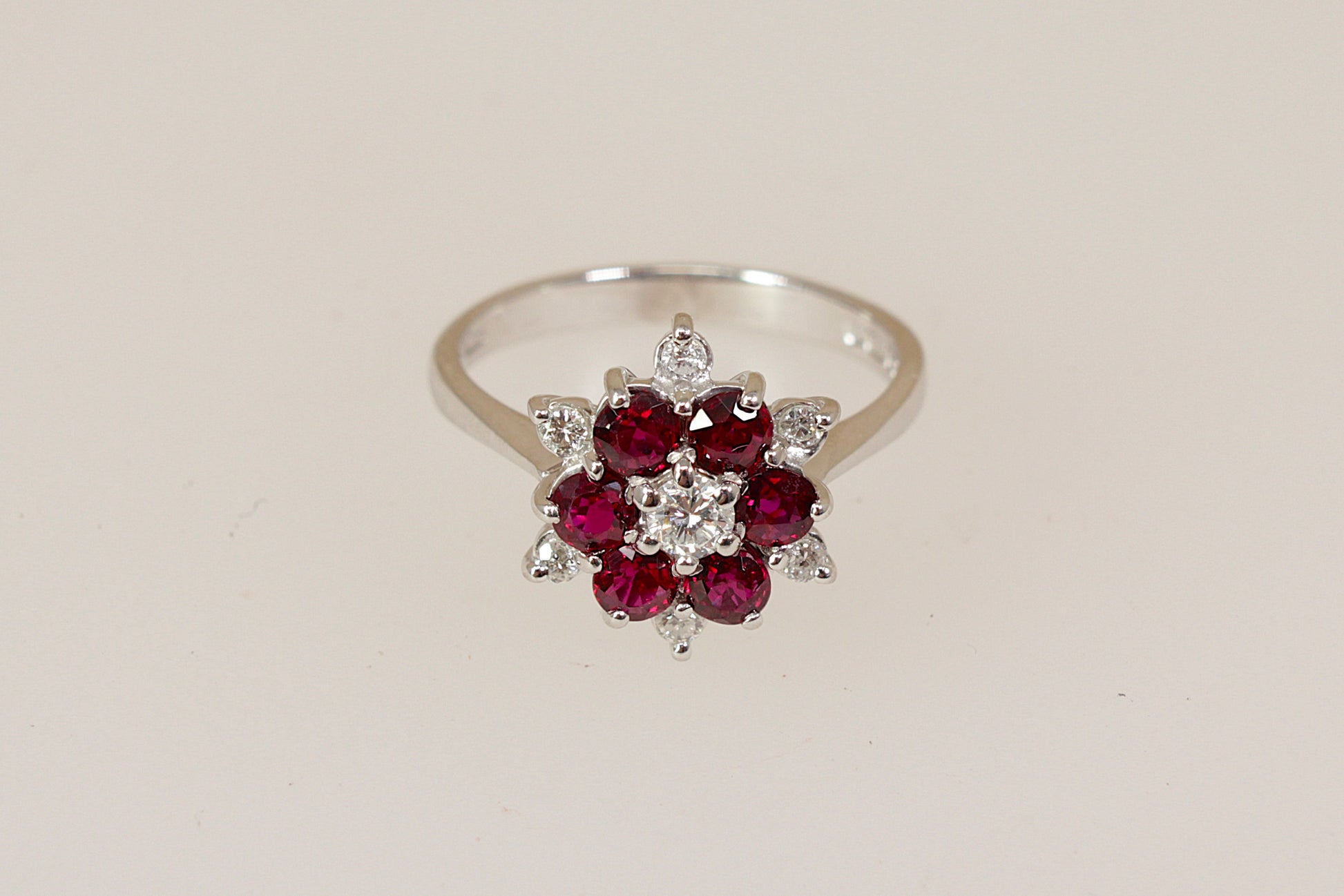 18ct white gold ring with rich red rubies and round brilliant diamond  gemstones on a beige background 