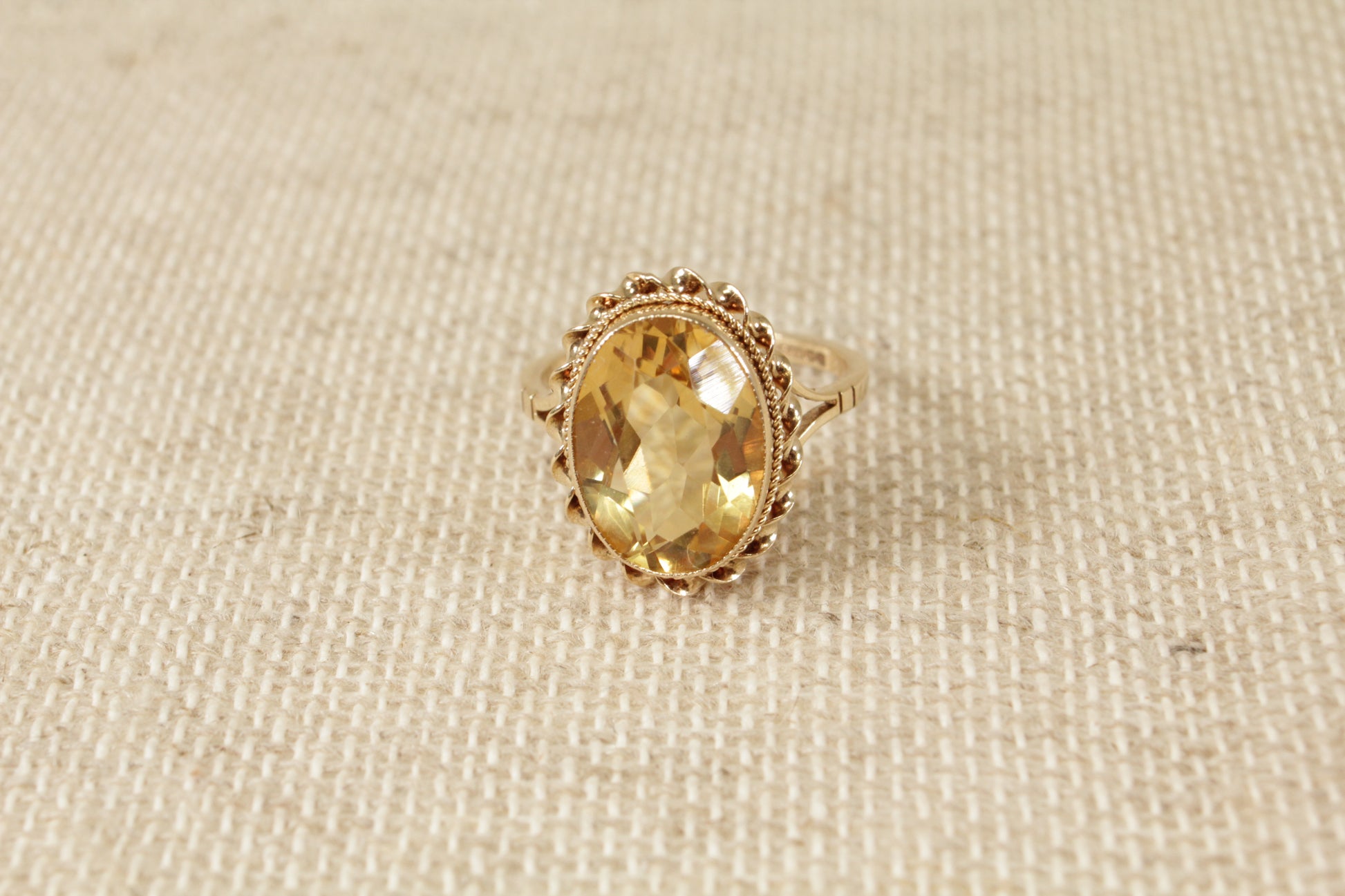 A vintage 9ct gold solitaire ring with an oval honey citrine gemstone, displayed against a textured background.