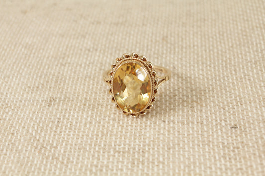 A vintage 9ct gold solitaire ring with an oval honey citrine gemstone, displayed against a textured background.