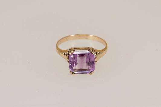 Gold ring with a purple amethyst gemstone on a beige background