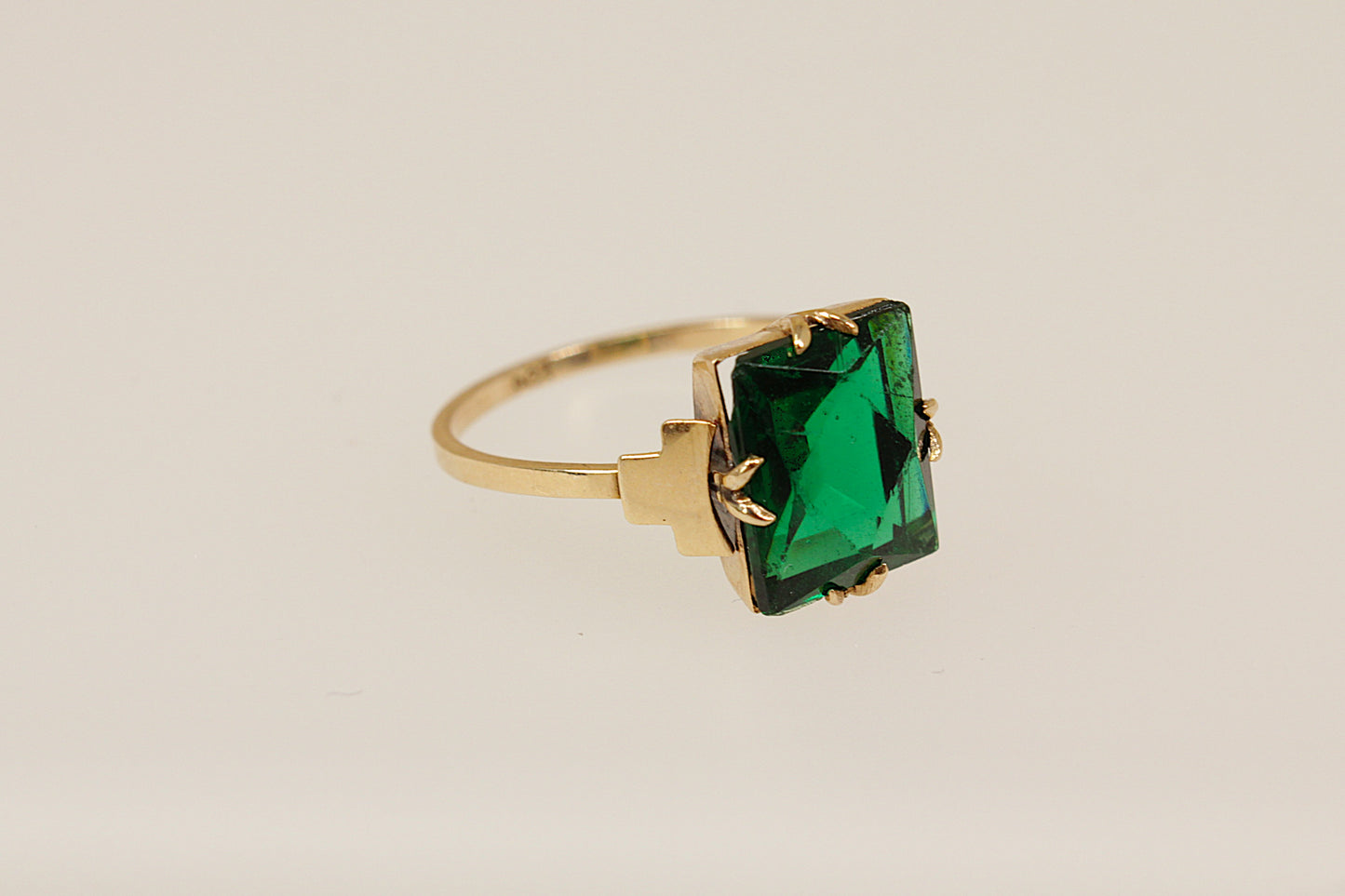 Gold ring with a green gemstone on a beige background