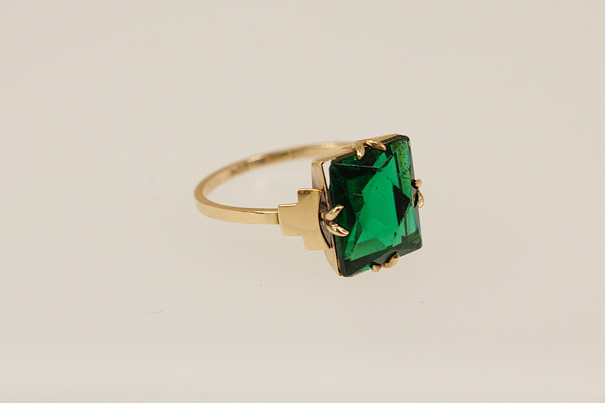 Gold ring with a green gemstone on a beige background