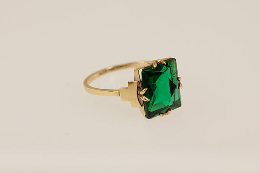 Gold ring with a green gemstone on a beige background