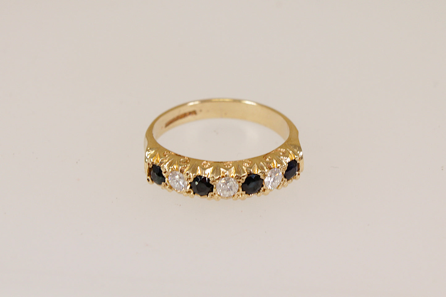 Yellow Gold ring with blue sapphires and clear diamond gemstones on a beige background