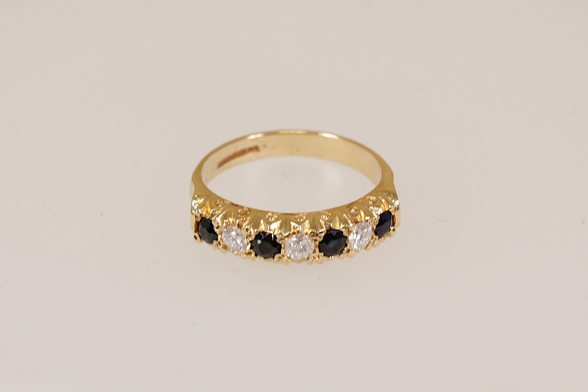 Yellow Gold ring with blue sapphires and clear diamond gemstones on a beige background