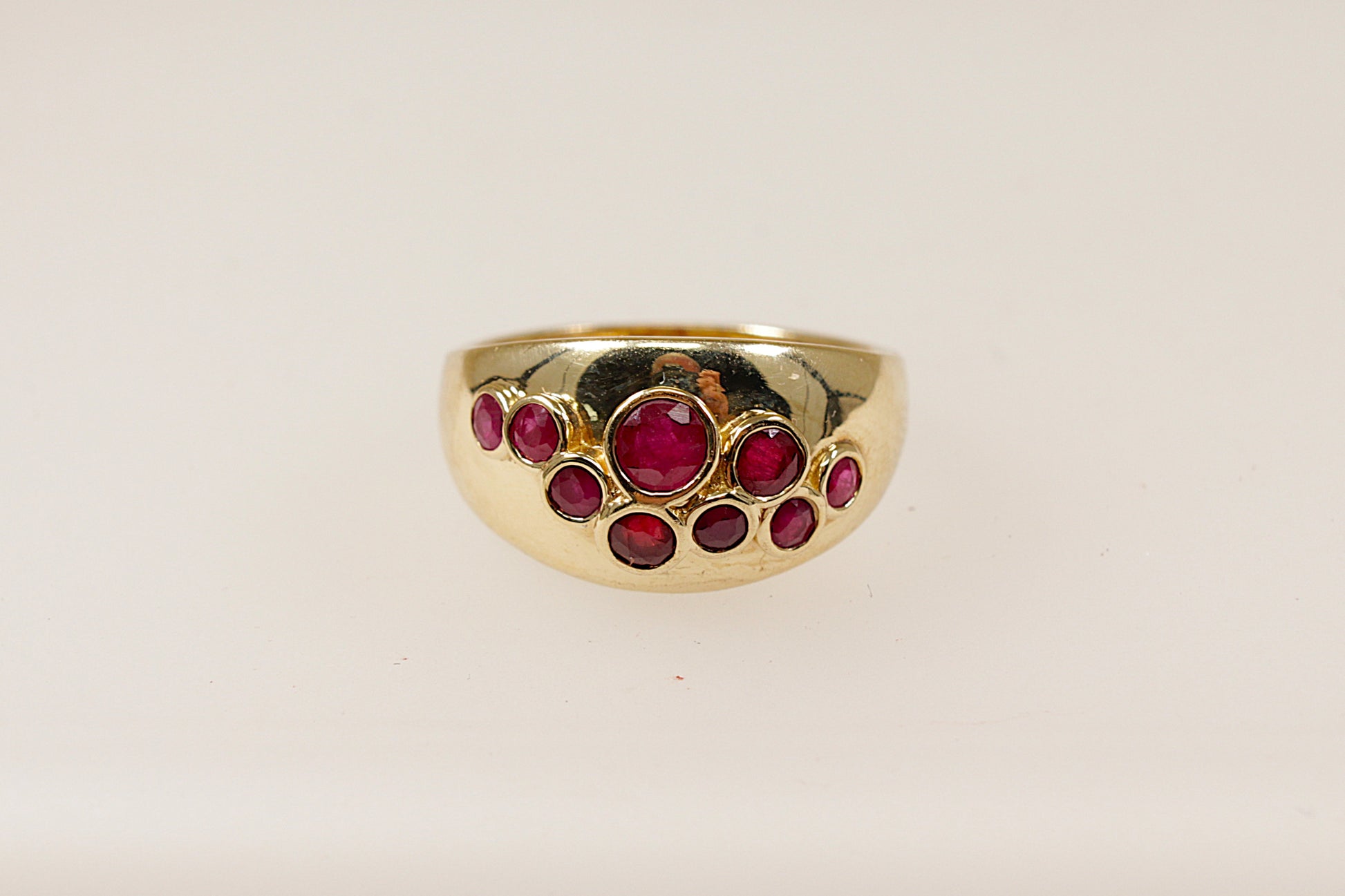A vintage 9ct yellow gold ruby scatter ring featuring nine bezel set ruby gemstones scattered across the head of the ring, the ring has full Birmingham hallmarks with the date letter for 1984, UK finger size O.