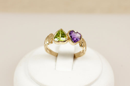 A delightful and symbolic 9ct gold ring, designed as a duo of bezel-set heart-shaped gemstones—a vibrant Peridot and a rich Amethyst, sitting side by side in perfect harmony. The design carries a romantic charm with a bold, confident presence, blending playful colour with classic elegance, UK finger size N.