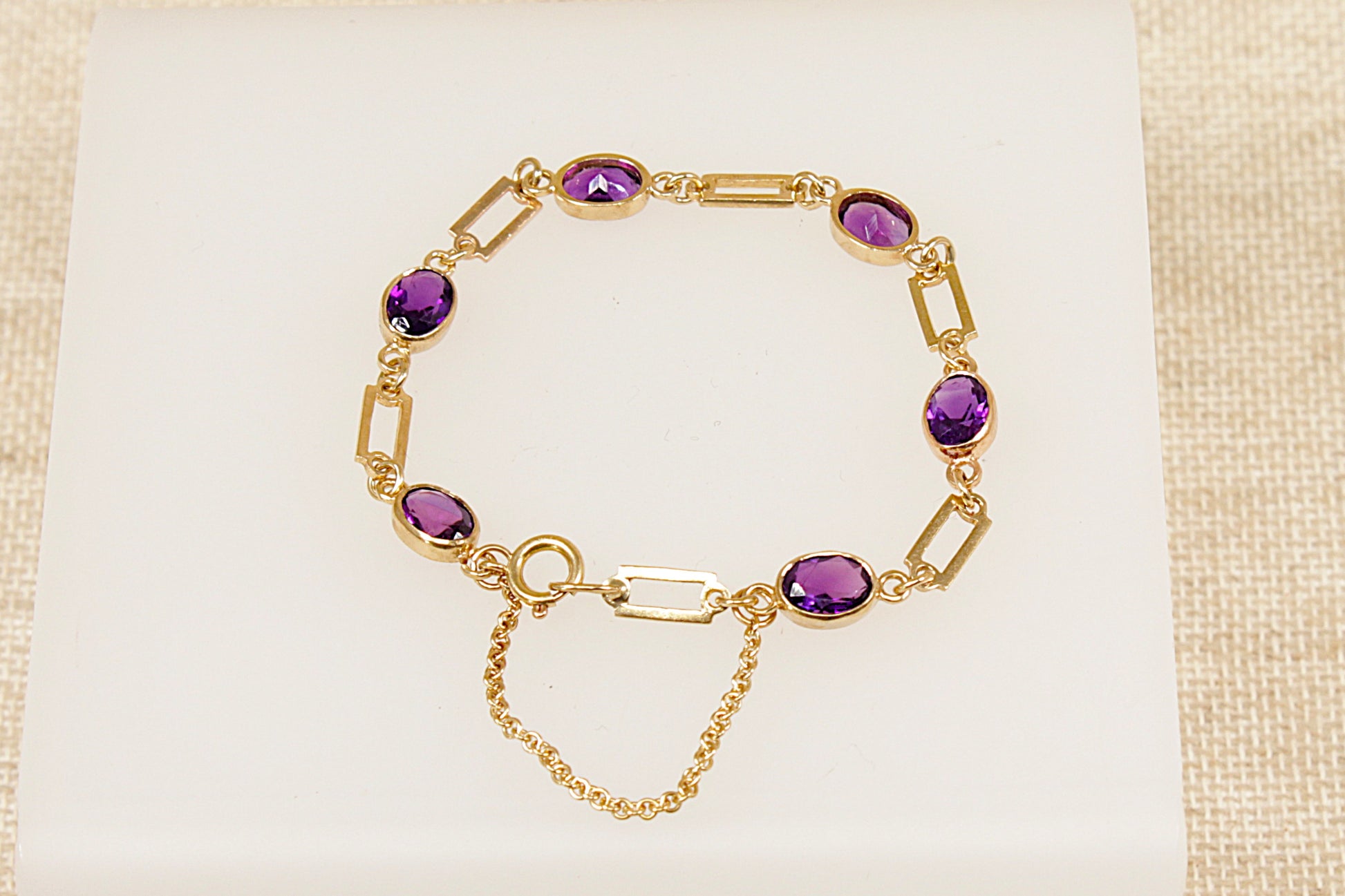 Gold bracelet with purple amethyst gemstones on a beige fabric background