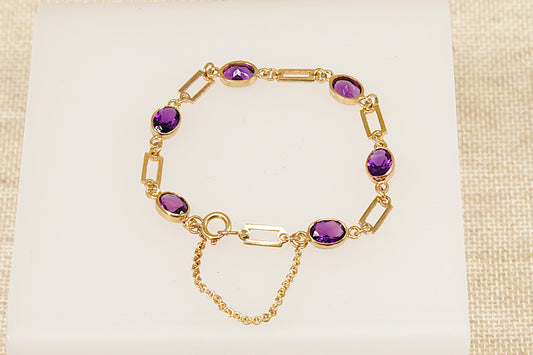 Gold bracelet with purple amethyst gemstones on a beige fabric background