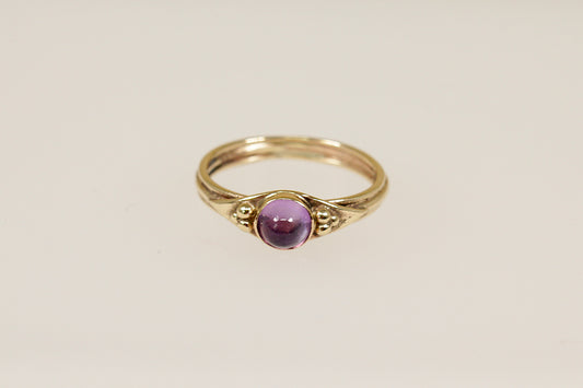 A vintage gold ring with a round amethyst cabochon gemstone set in a 9ct gold band with hallmarks interior.