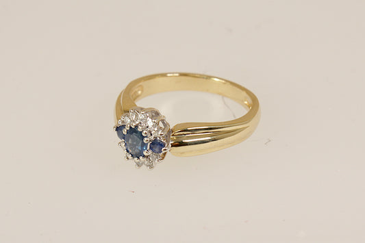 9ct Gold Sapphire and Diamond Cluster Ring, A beautiful and distinctive 9ct Gold ring, showcasing an interesting and elegant design. At its heart is a vibrant oval Blue Sapphire, flanked by two round Blue Sapphires, forming a rich and regal trilogy centrepiece. it bears full London hallmarks for 1993, confirming its gold purity and vintage authenticity, perfect as a unique engagement ring, UK Finger size: O.