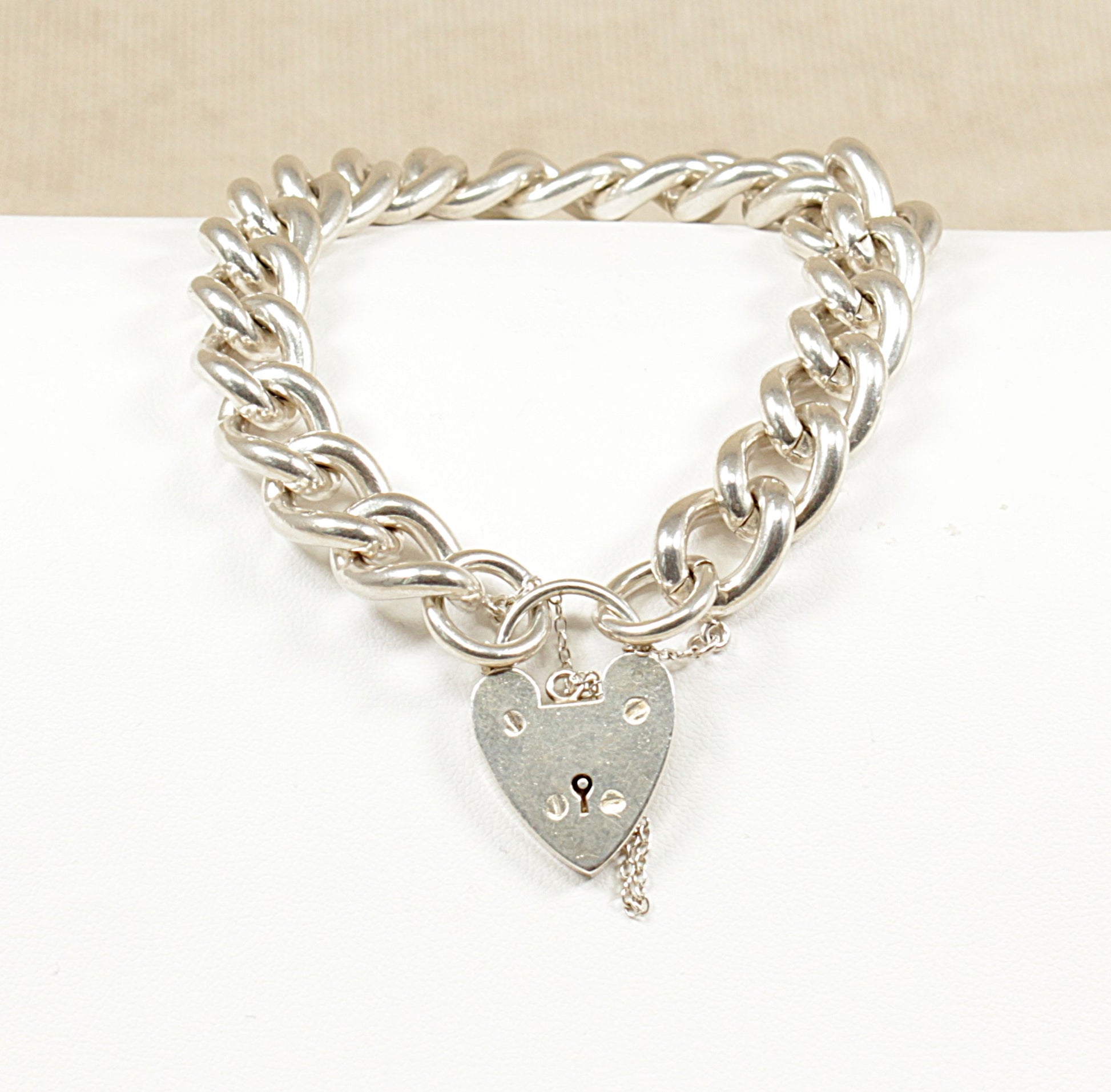 A vintage silver curb link bracelet with a padlock clasp, displayed against a beige background.