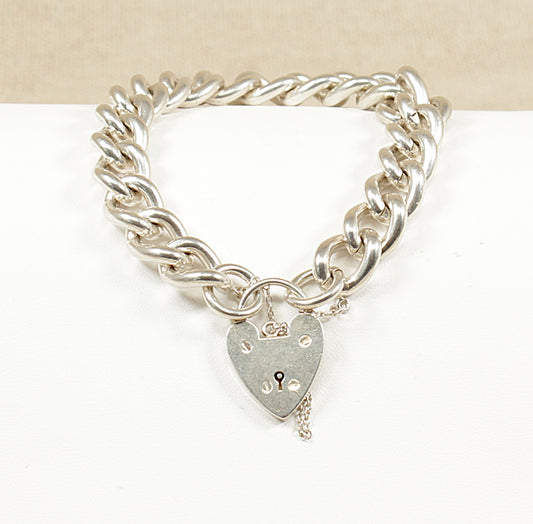 A vintage silver curb link bracelet with a padlock clasp, displayed against a beige background.